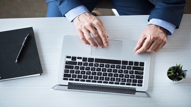 Cropped view of businessman working with laptop on workplace in office