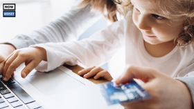 A little girl sits on her parent's lap and observes while the parent makes an online purchase.