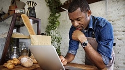 7 steps to getting a business loan african american male looking at laptop in his bakery shop