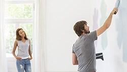 Take on a Home Improvement Project Man is paiting a wall while woman is watching