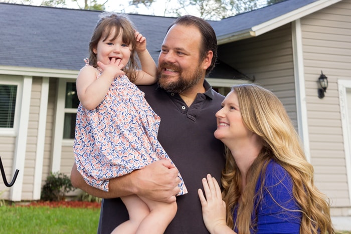 How I found love—and fixed my finances Man holding daughter alongside his wife in front of hom.