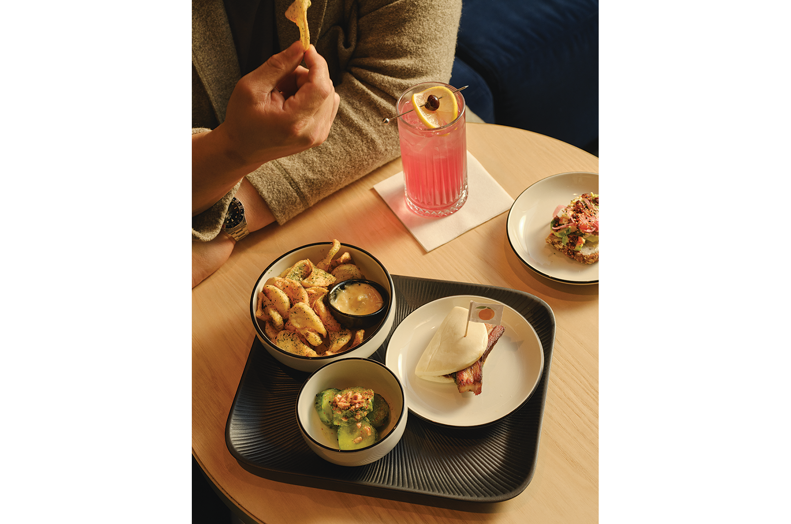 Table with seasoned fries, bao bun, salad, and a pink drink garnished with citrus and cherry.