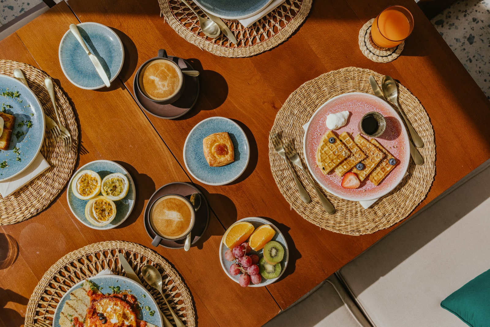 Plates of assorted fruits, eggs, and lattes sit in an attractive array on a dining table.