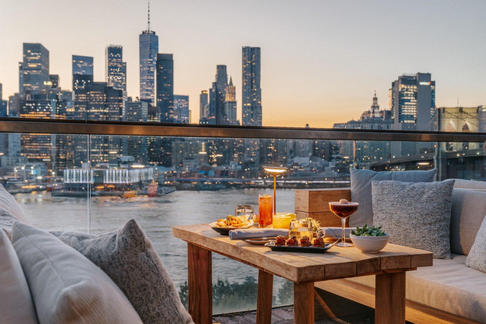 A table set with food and two outdoor sofas at a rooftop lounge.