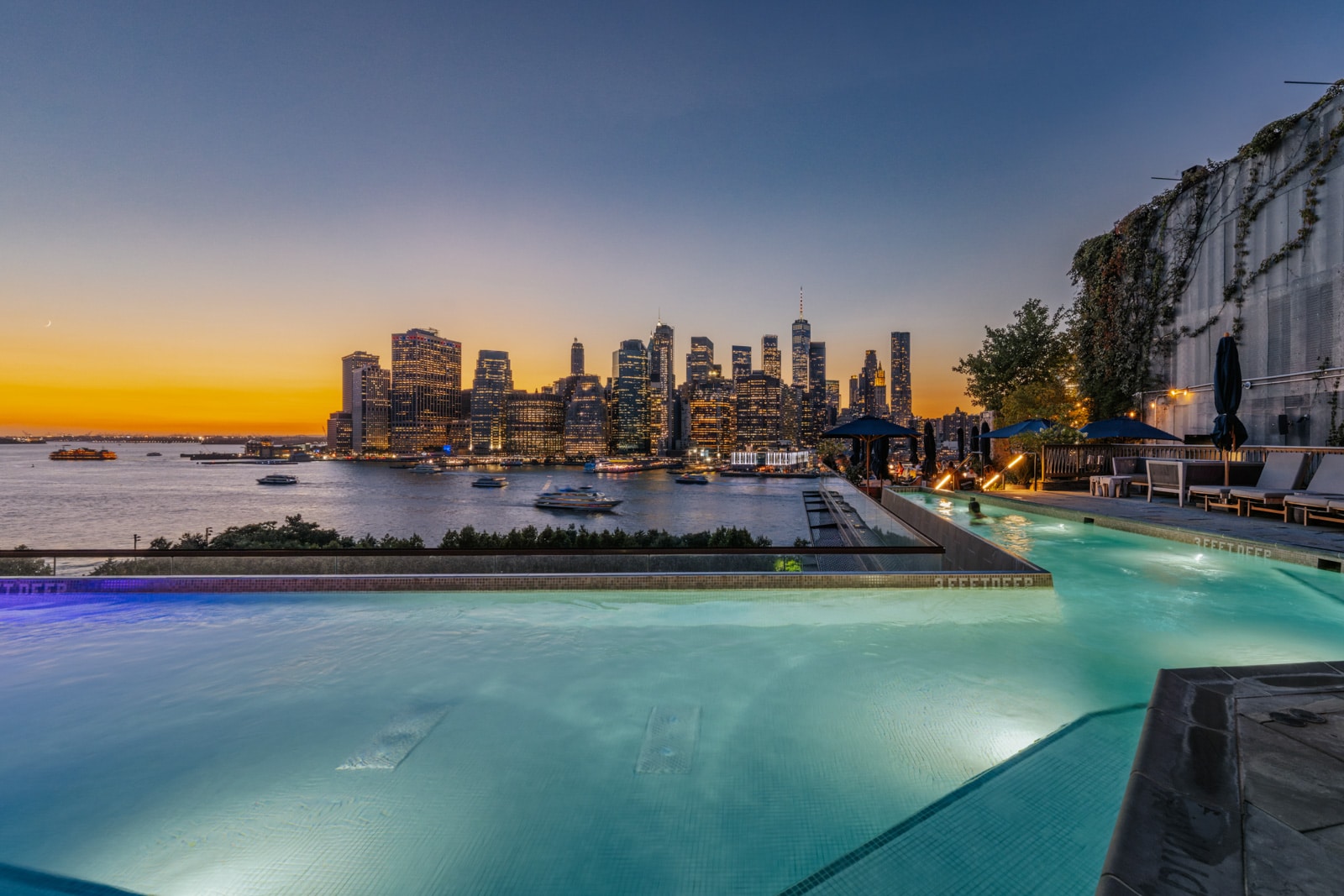 A pool overlooks the East River Estuary and Financial District in New York City during sunset.