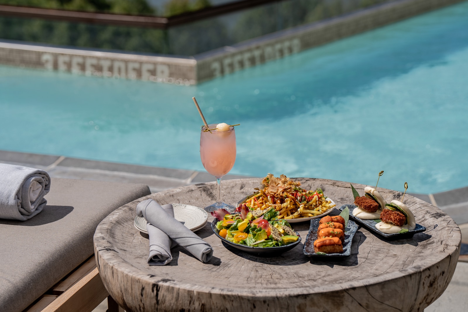 Plates of food and a beverage at an outdoor table near a pool.