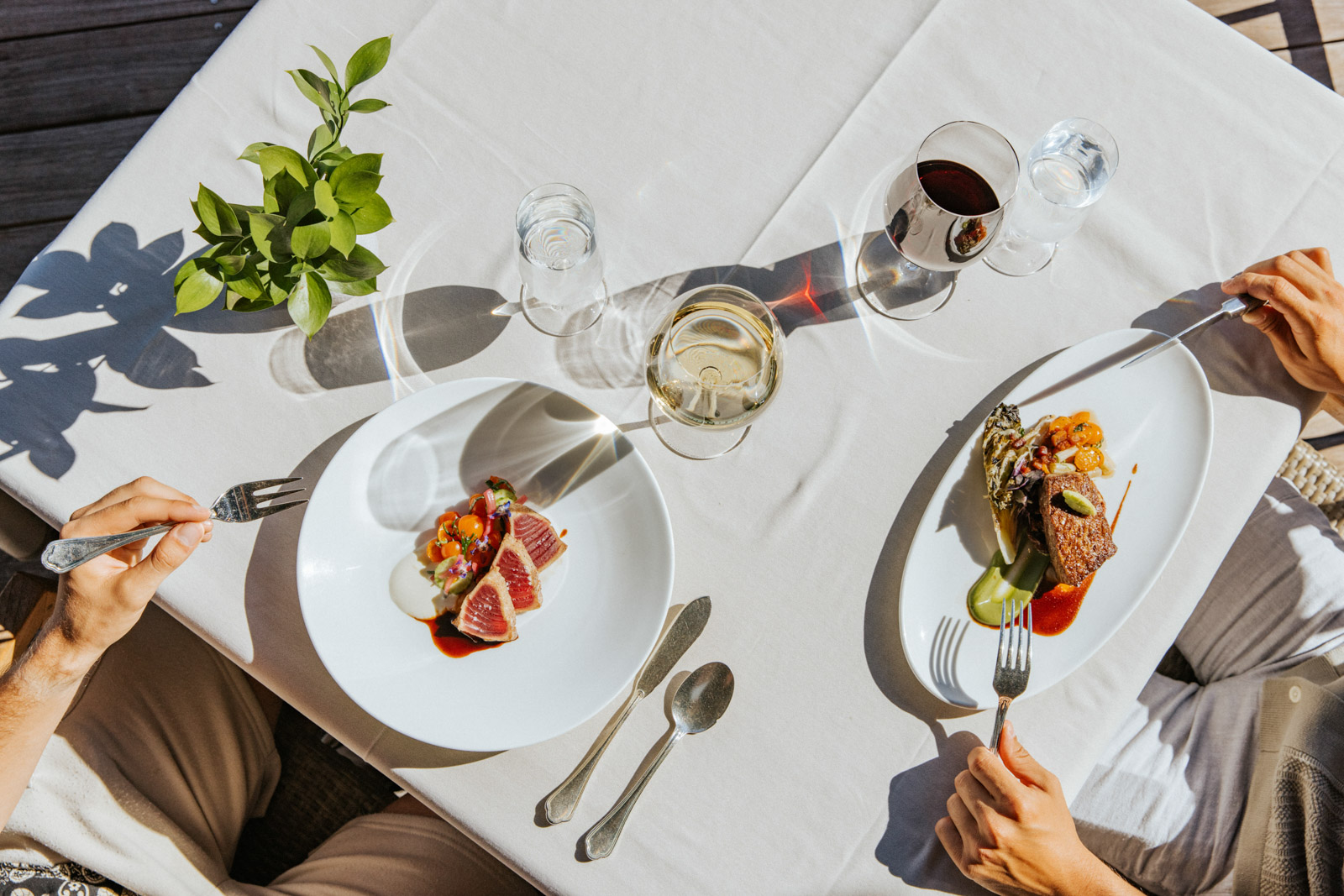 Two people sit at a table eating food with glasses of white and red wine