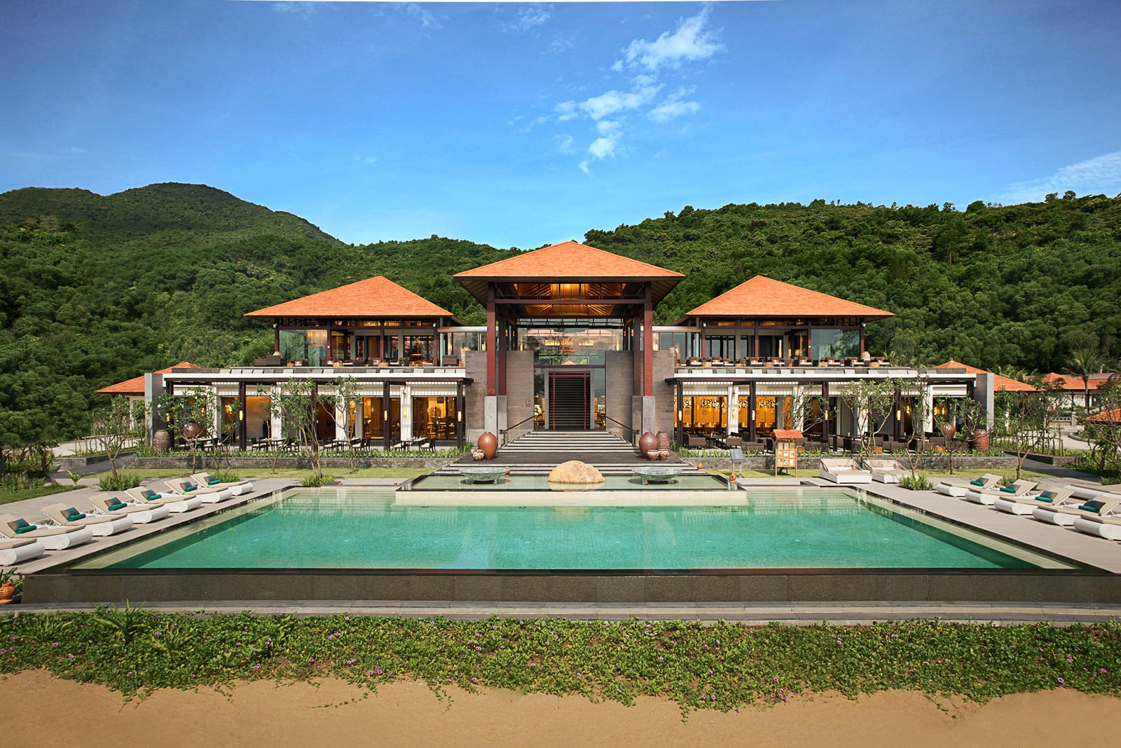 A large pool surrounded by lounge chairs abuts the beach.