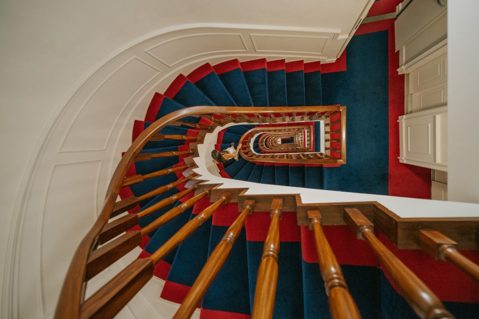 Looking down a winding spiral staircase with wooden railings and blue and red carpeting in a stylish interior.