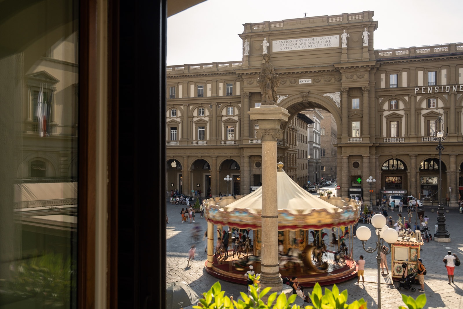 A view of a carousel in a piazza through an open window.