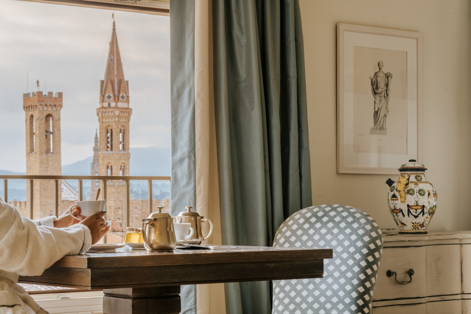 A person sits at a table enjoying tea, looking toward the Duomo in Florence through a window.