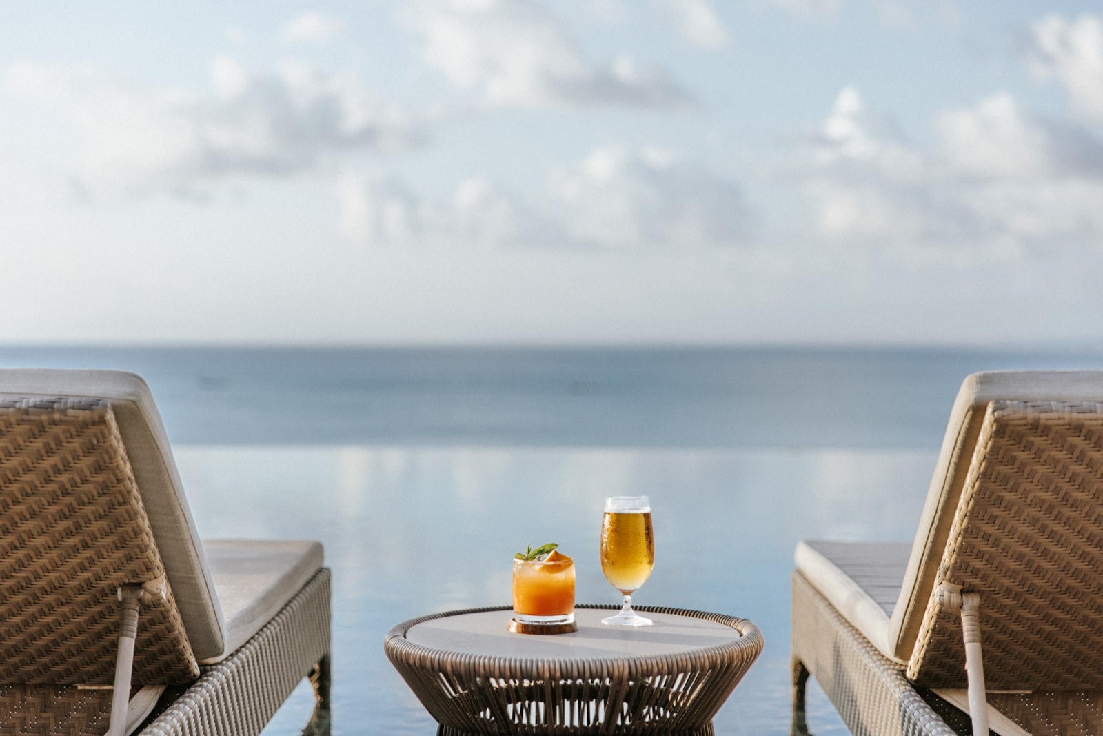 Two lounge chairs by an infinity pool with drinks, facing the ocean horizon.