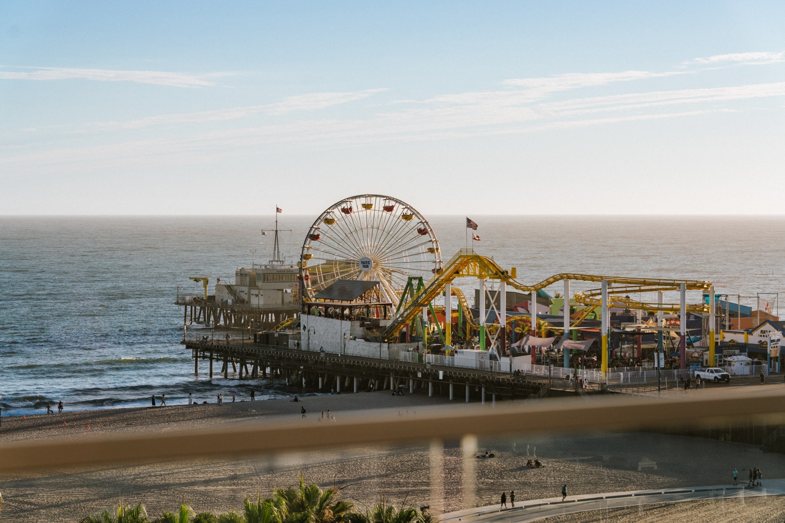 Daytime view of Santa Monica Pier with Ferris wheel and yellow coaster above the shimmering sea.