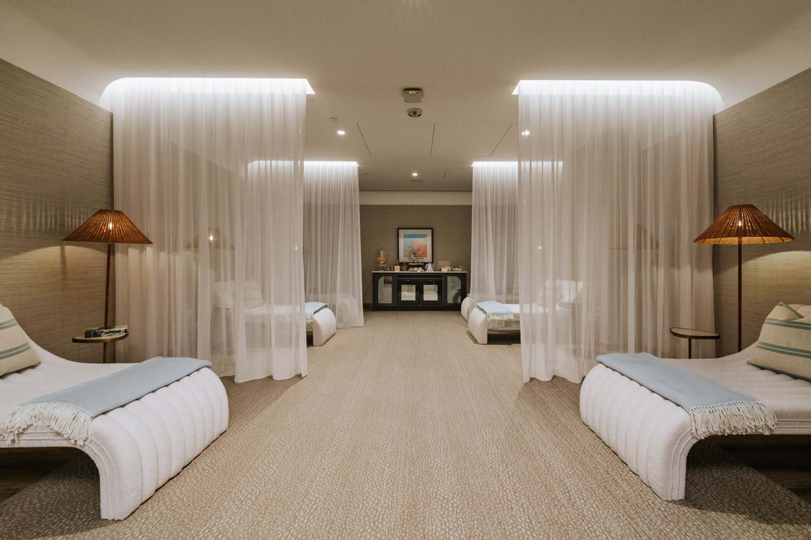 Serene spa lounge with white chaise beds, sheer curtains, and soft amber lamps in warm neutrals.