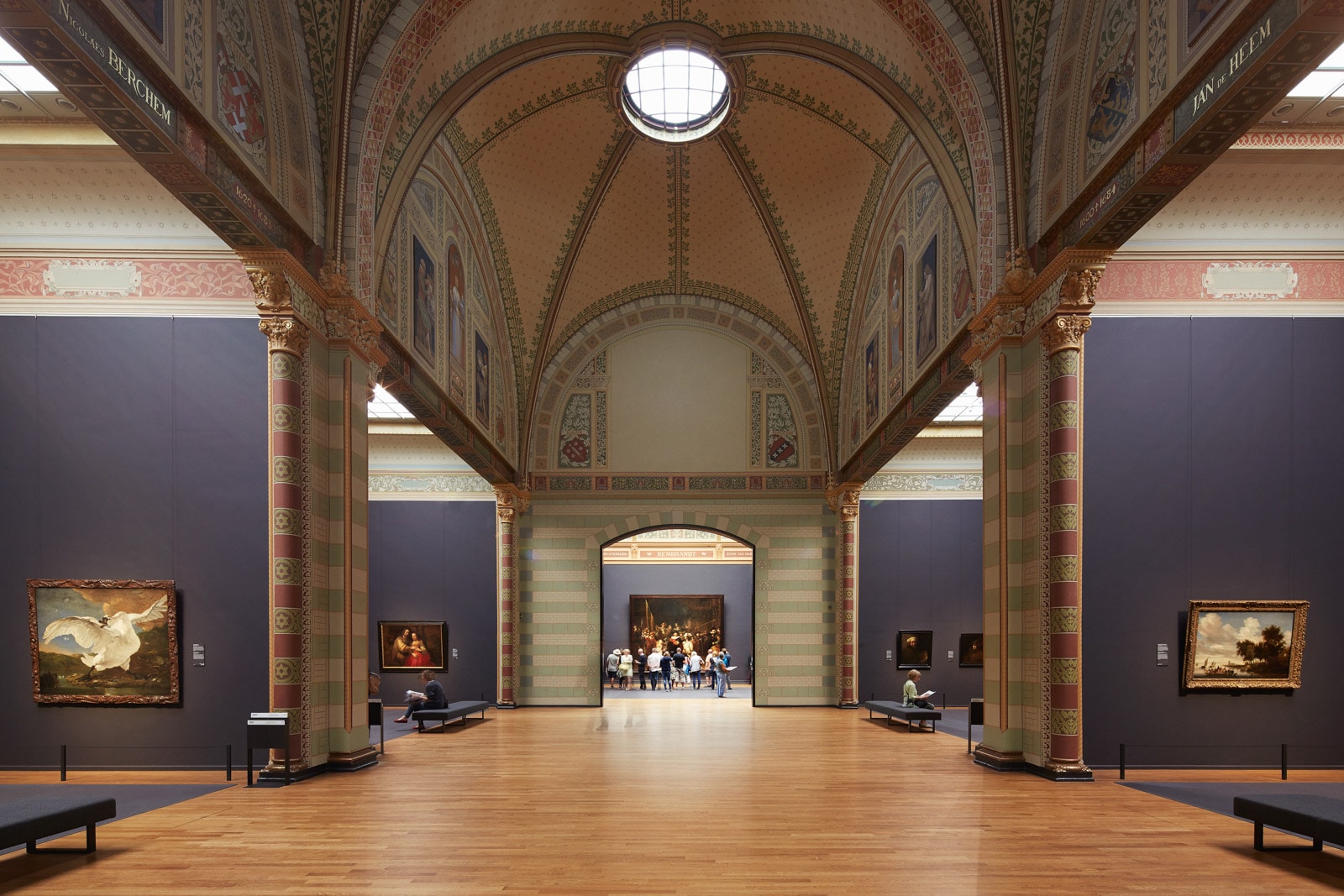 Ornate museum gallery with high ceilings, columns, and framed paintings on the walls.