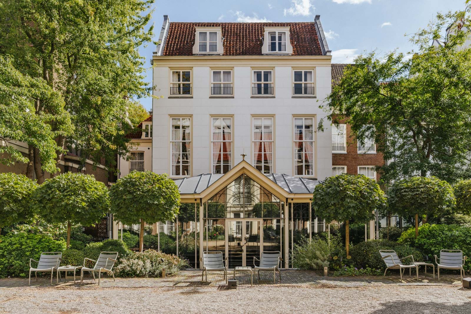 Elegant white townhouse with a garden and outdoor seating surrounded by trees.
