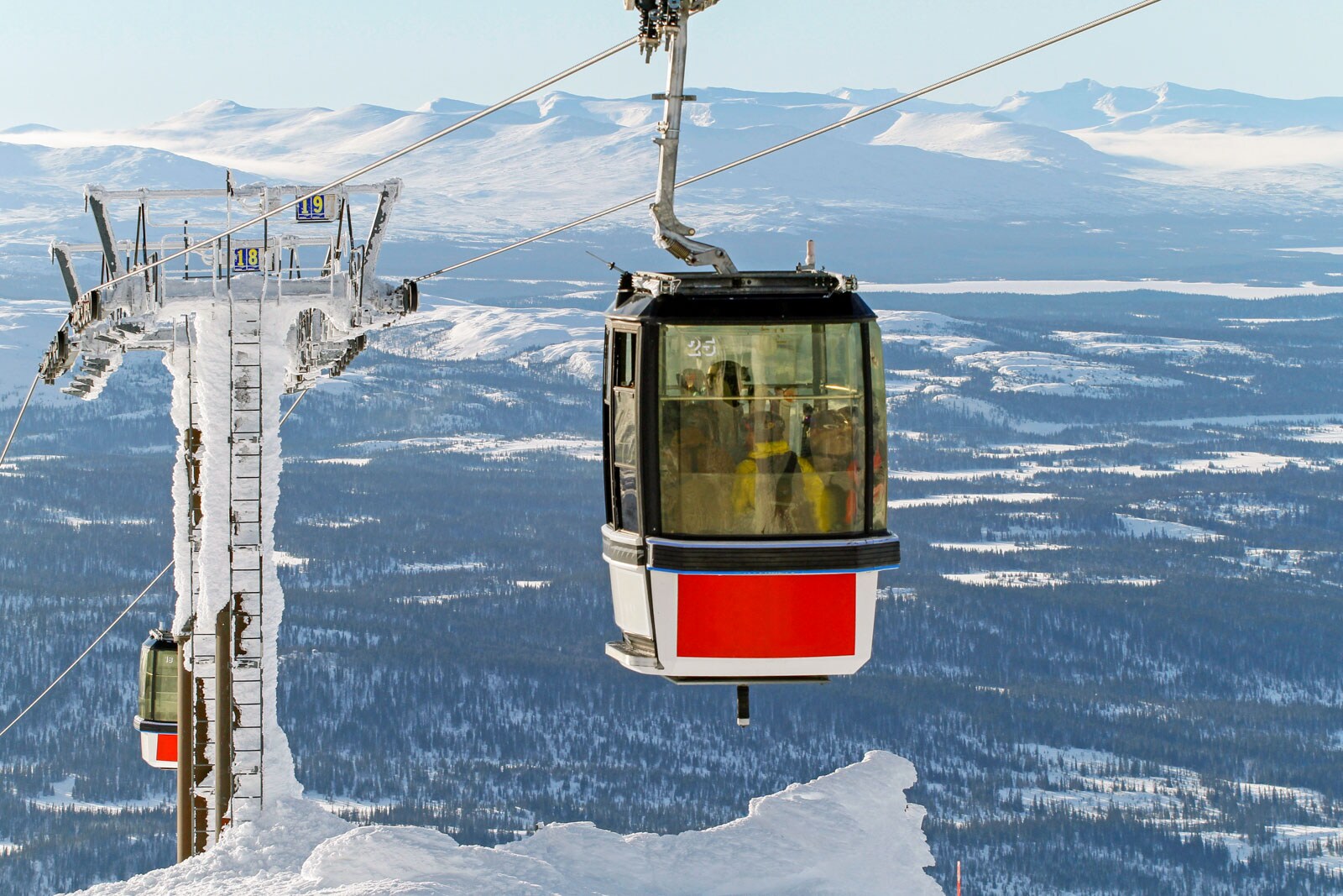 Red and white cable car suspended on a snowy mountain, with panoramic views of snow-covered hills and distant peaks.