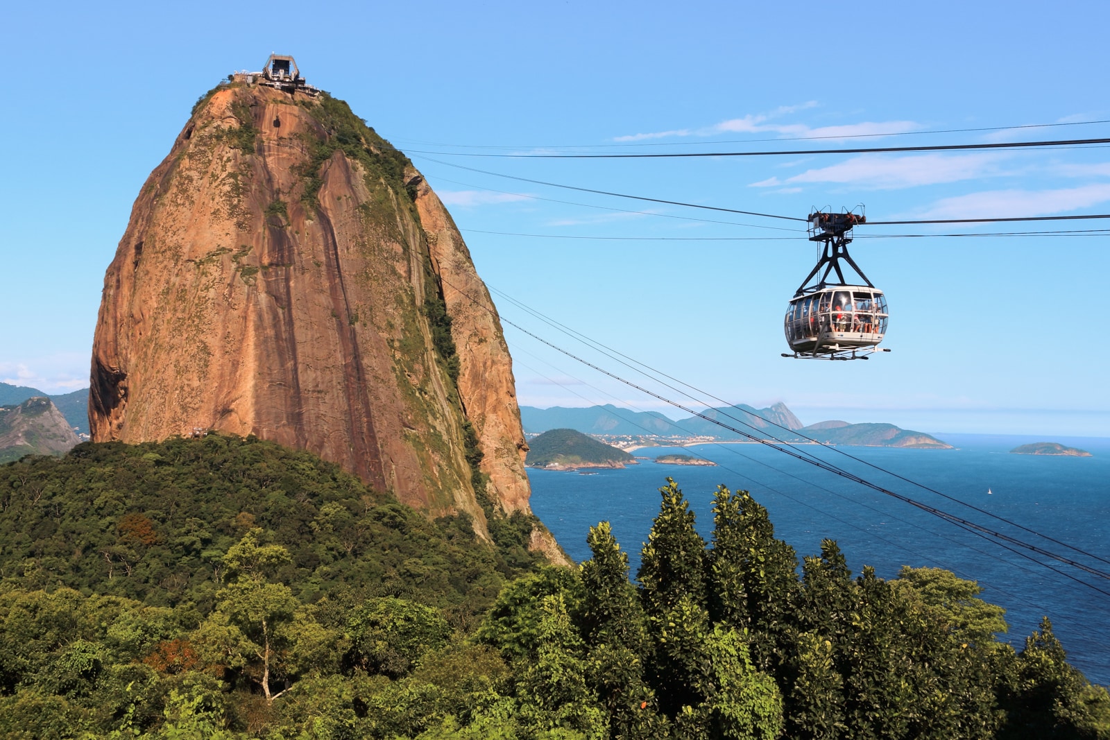 Cable car glides past Sugarloaf Mountain over deep blue sea under a bright sky.