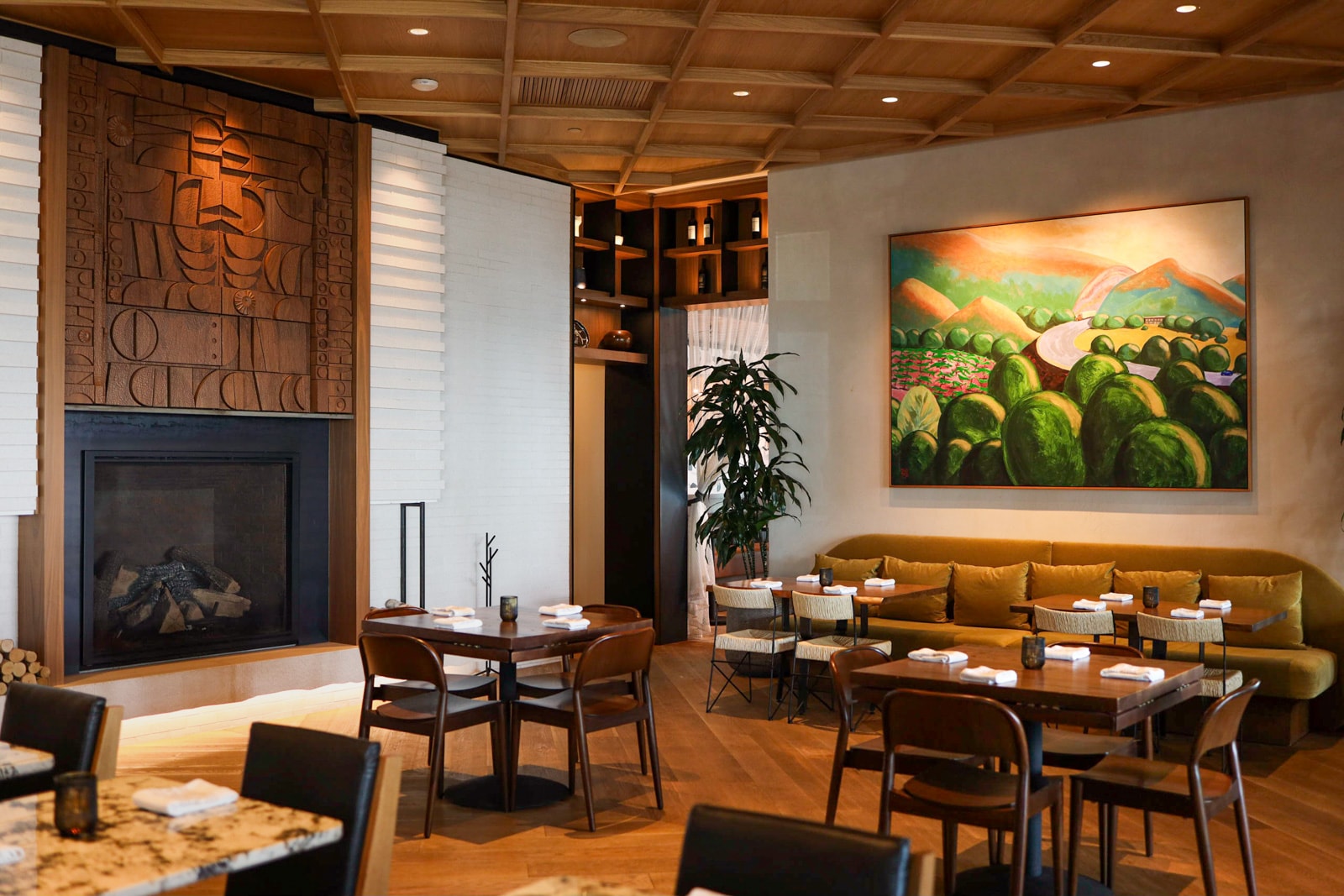 Warm modern dining room with wood ceiling, green landscape art, and mustard sofa.