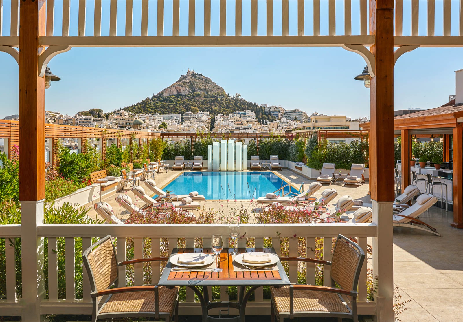 A view from the pool deck of a hotel in Athens shows the city beyond and ruins on a hilltop.