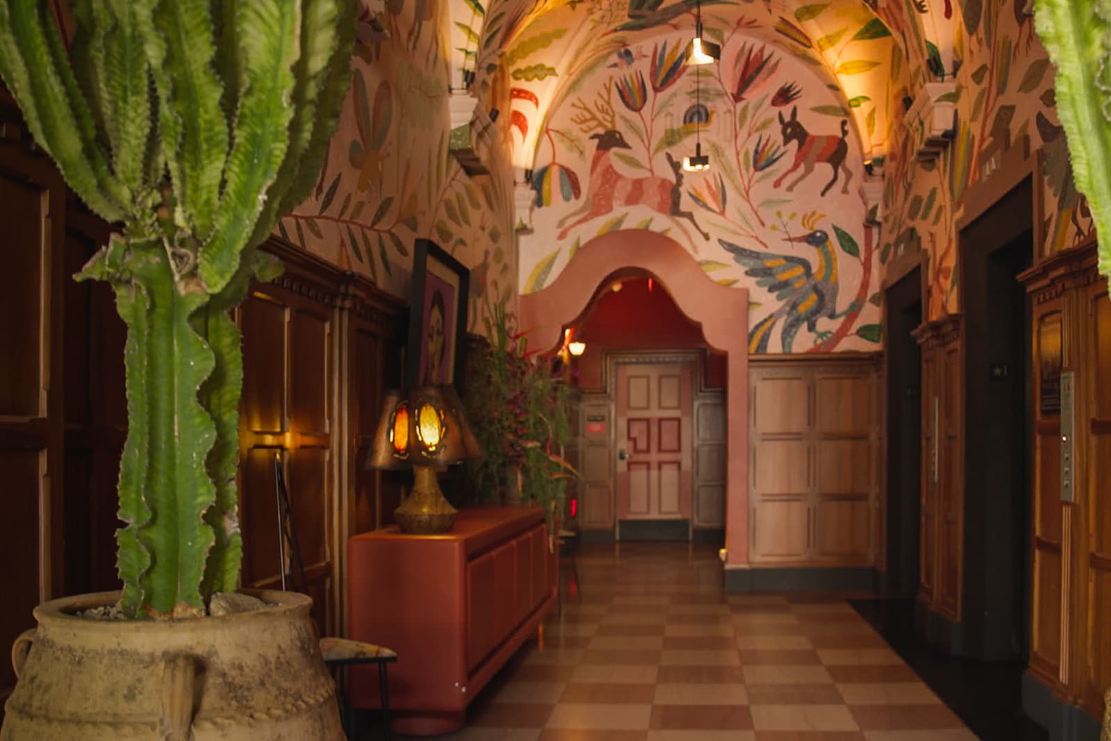 The reception area of LA Proper Hotel features murals on a vaulted ceiling and potted cactus plants.
