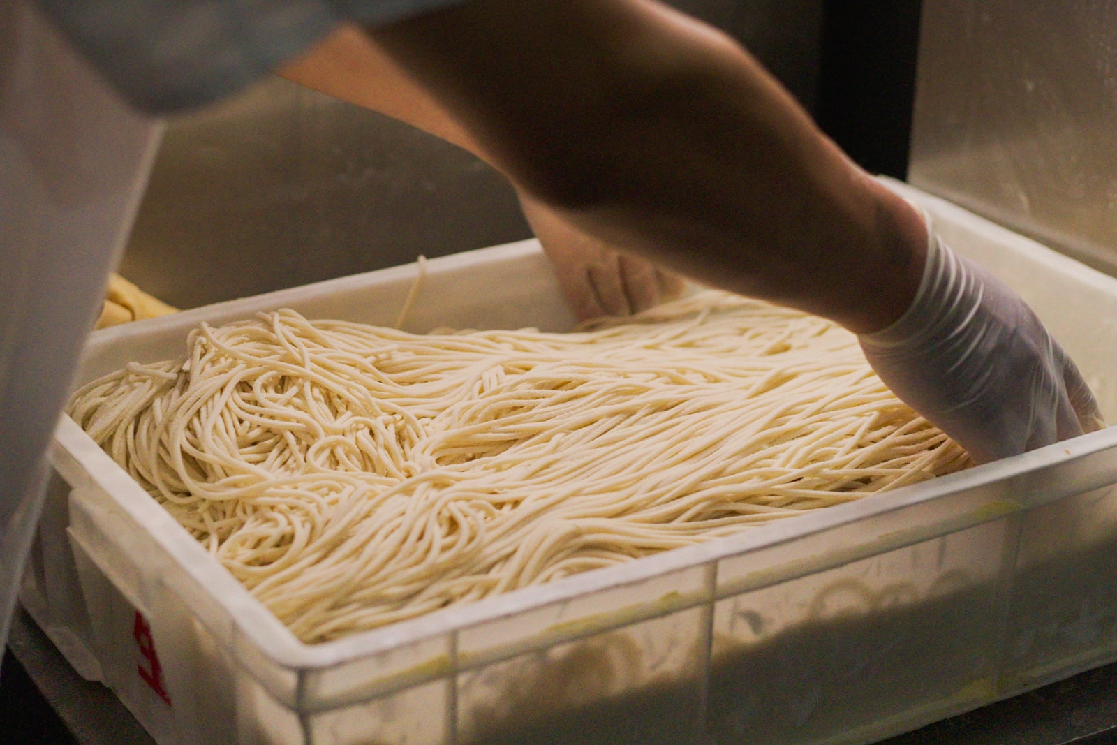 A person prepares noodles in a plastic tub.