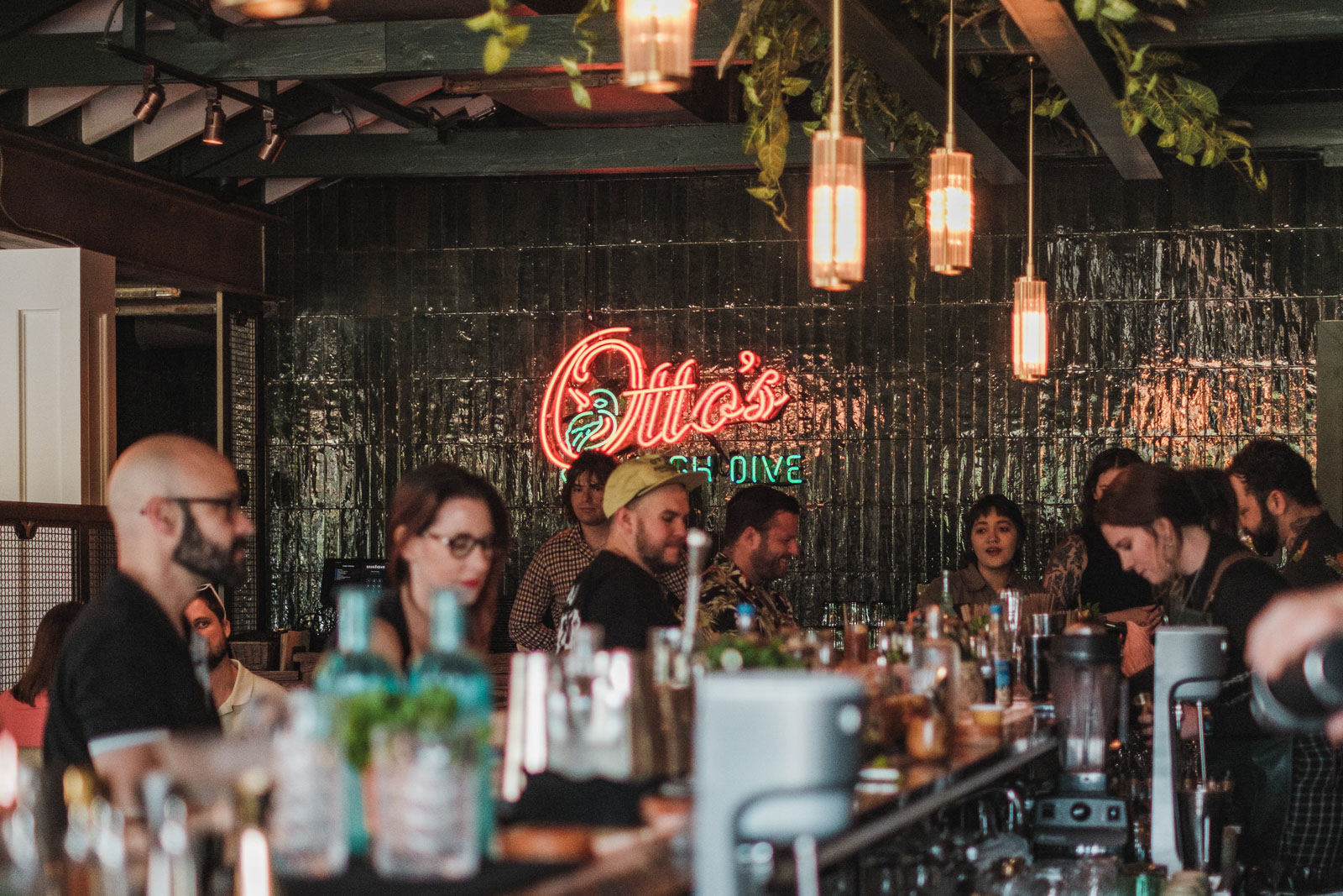 People sit at a bar under a neon sign reading Otto's.