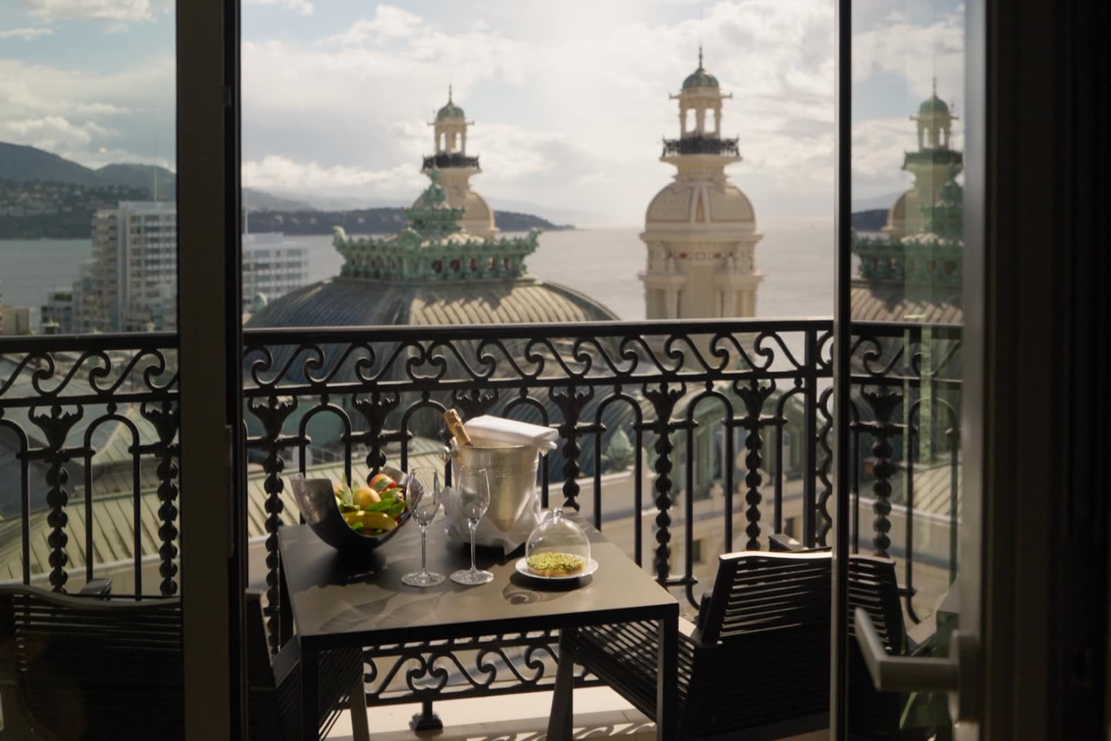 A dish of fruit and some chilled champagne sit atop a table on a balcony.