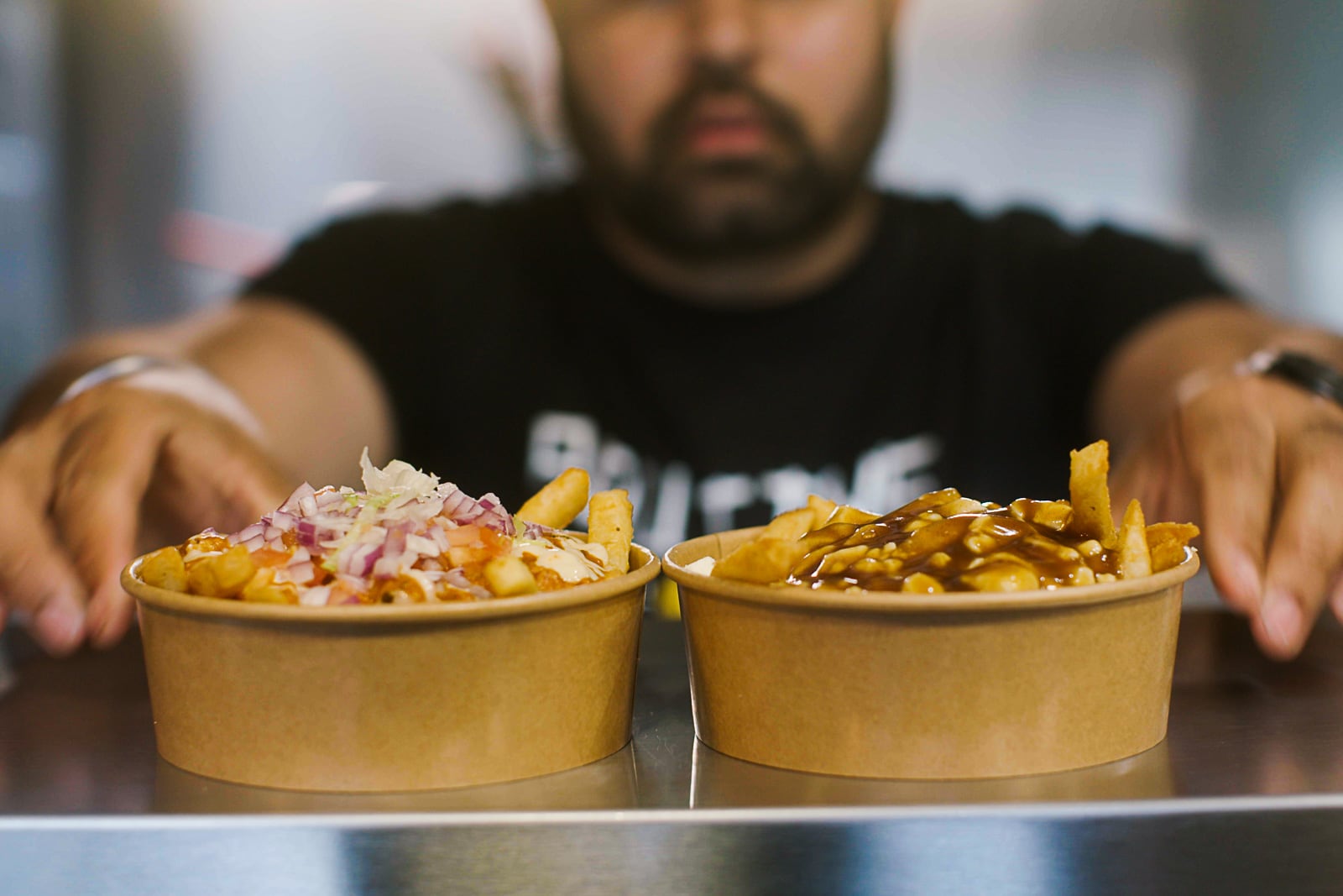 A chef presents two cardboard bowls filled with poutine, a popular dish in Canada made with fried potatoes.