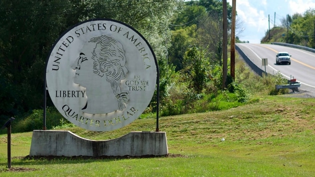 The image shows a sign saying United States of America Quarter Dollar on the side of a highway. 